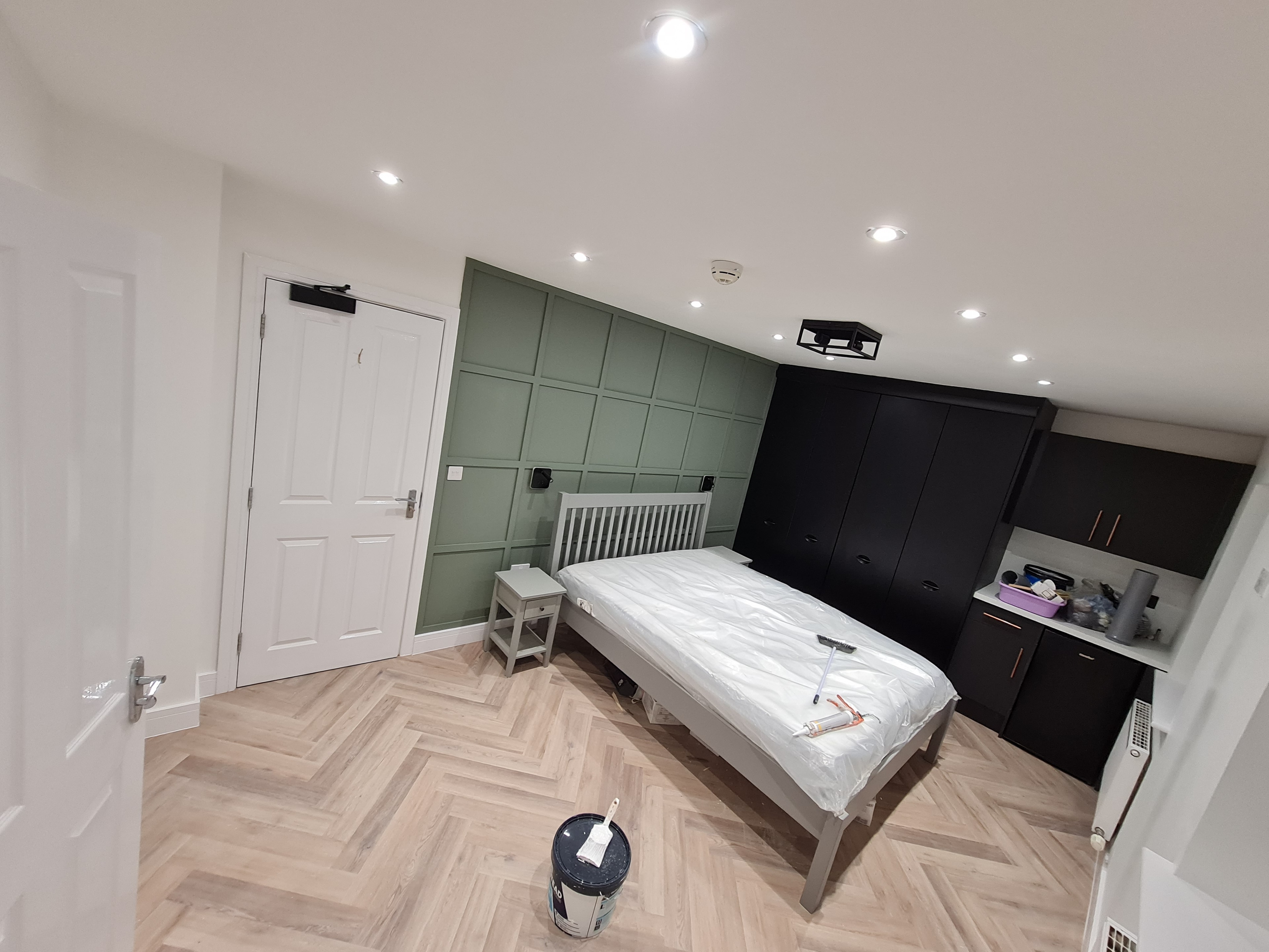 Black kitchen units with green feature wall and herringbone flooring
