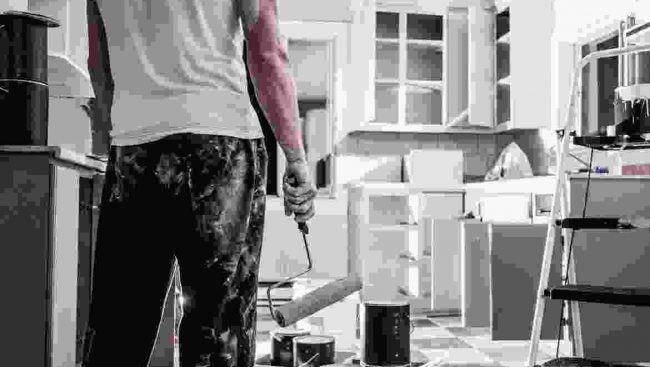 A man standing in a kitchen with a paint roller.