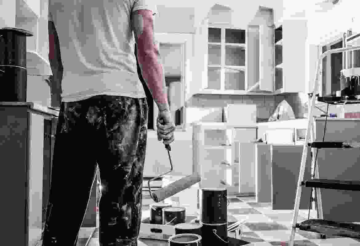 A man standing in a kitchen with a paint roller.