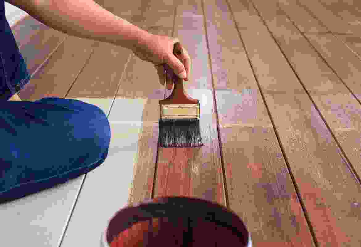 A person painting a wooden floor with a paint brush.