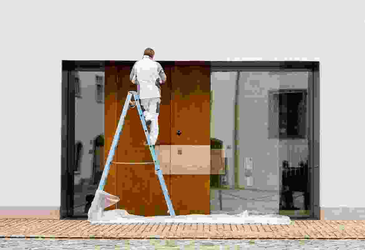 A man on a ladder painting a wooden door.