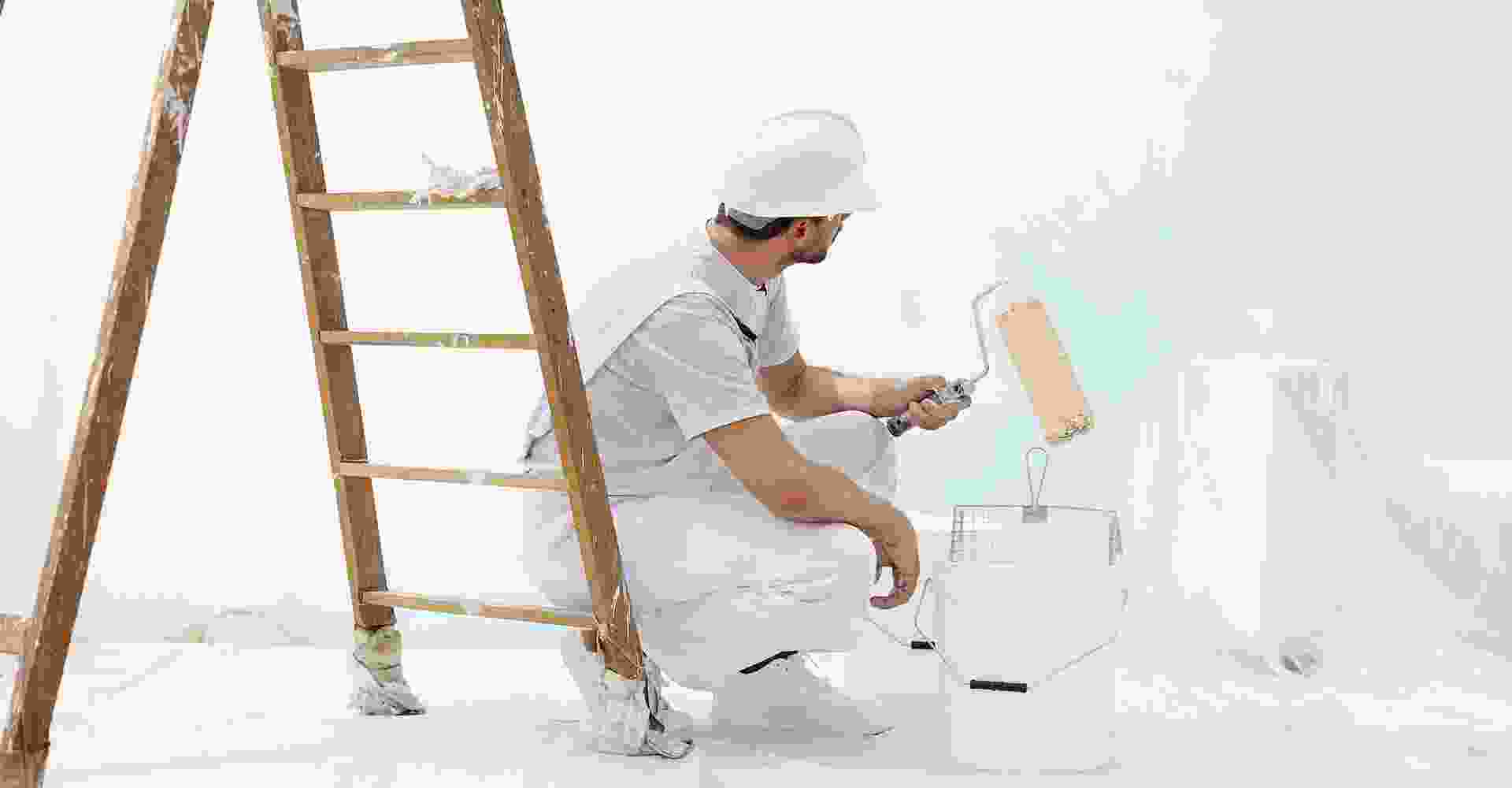 A man painting a white room with a ladder.