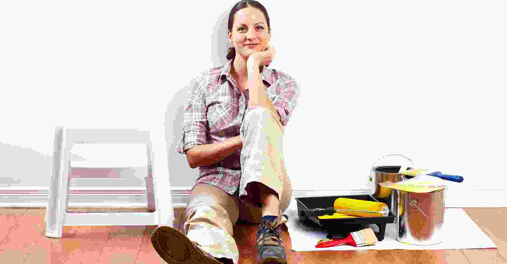 A woman sitting on the floor with paint tools.