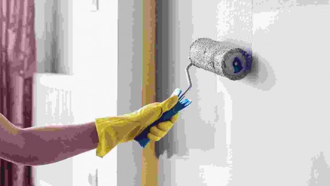 A woman is painting a wall with a paint roller.