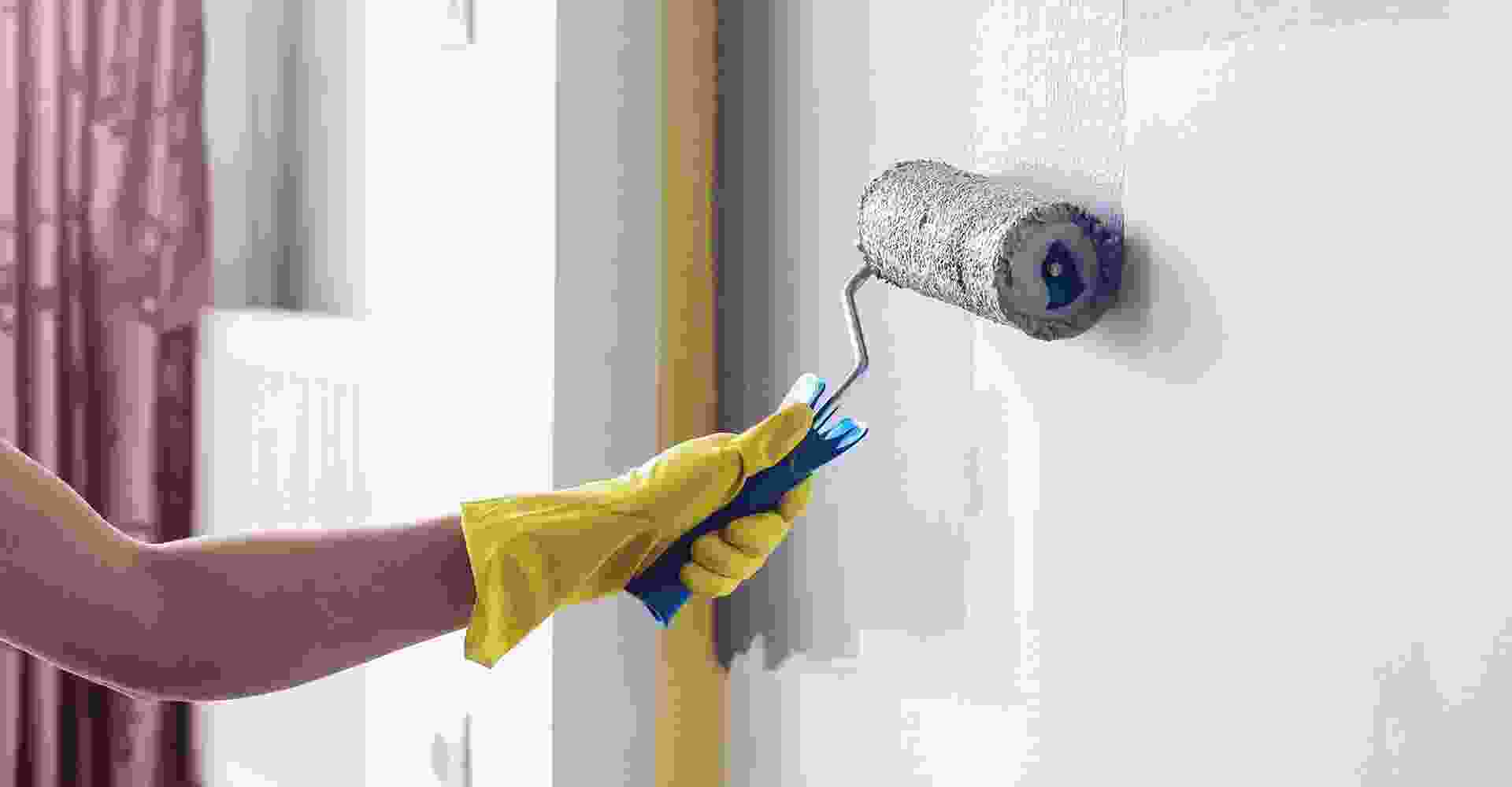 A woman is painting a wall with a paint roller.