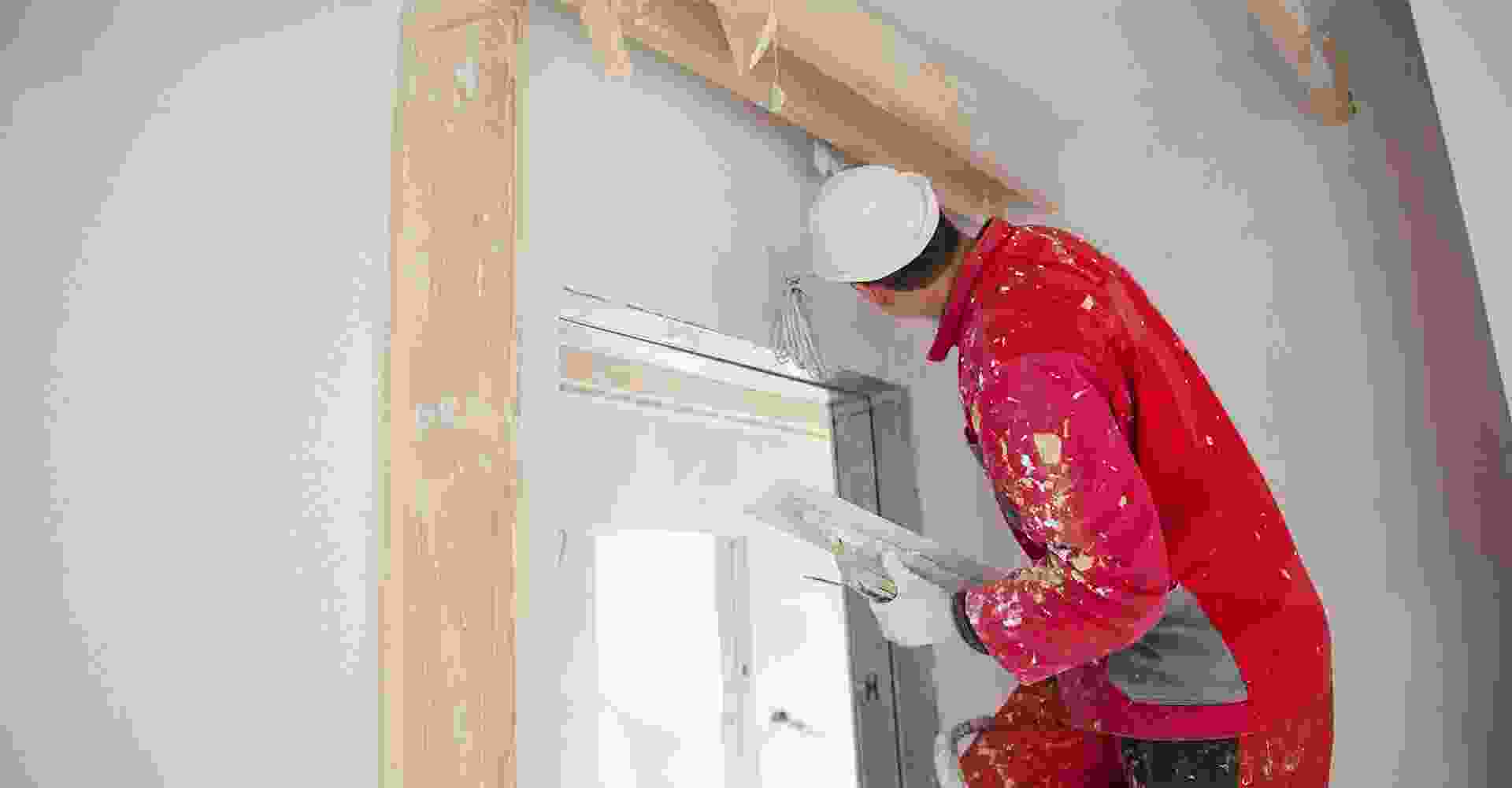 A man in a red jacket is painting a door.