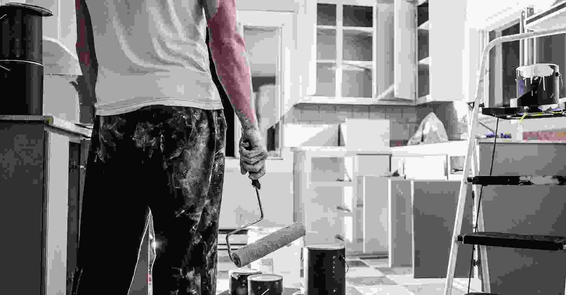 A man standing in a kitchen with a paint roller.