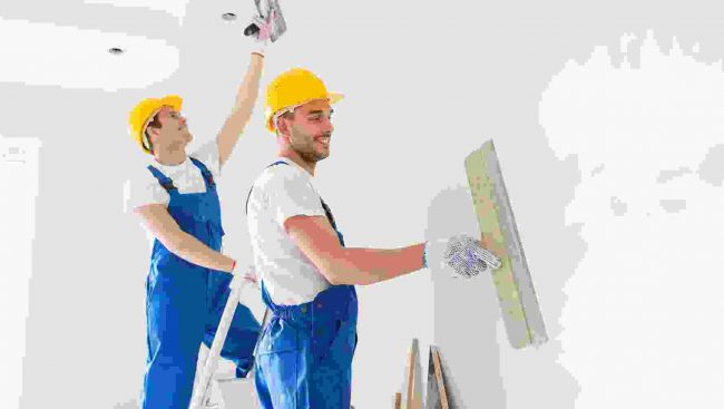 Two men in hard hats working on a wall.