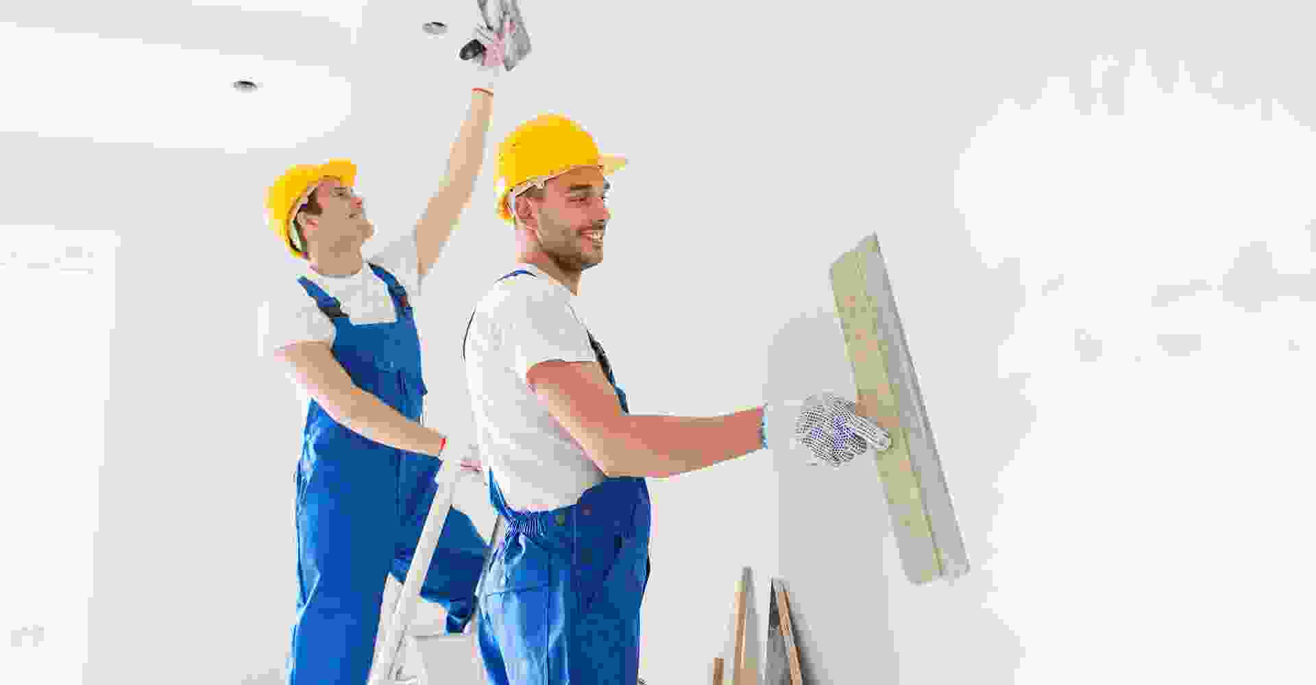 Two men in hard hats working on a wall.