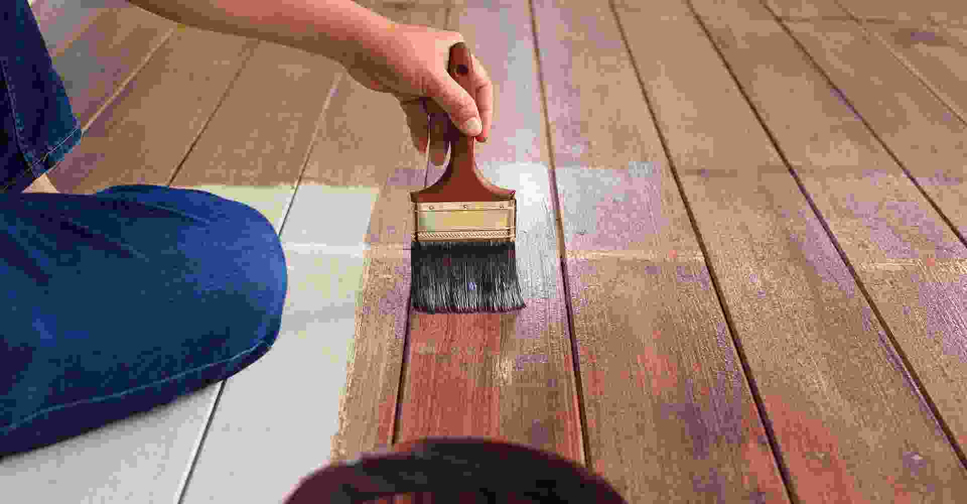 A person painting a wooden floor with a brush.