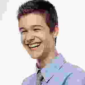 A young man in a blue shirt and tie is smiling.