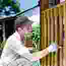 A man painting a wooden fence in front of a house.