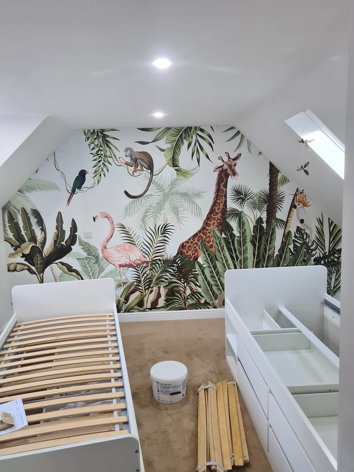A child's bedroom with a mural of giraffes and flamingos.