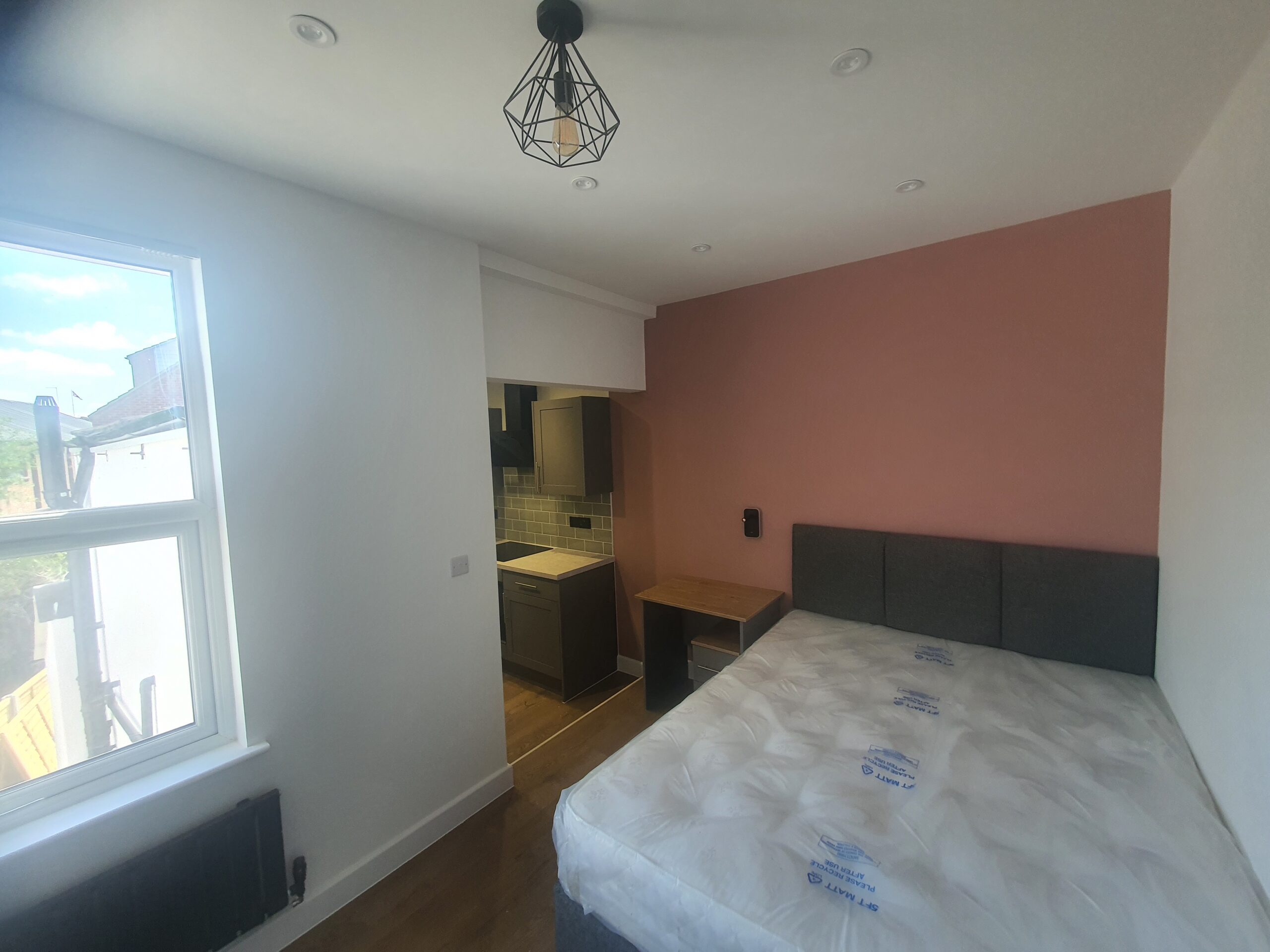 A bedroom with a bed, desk and window.