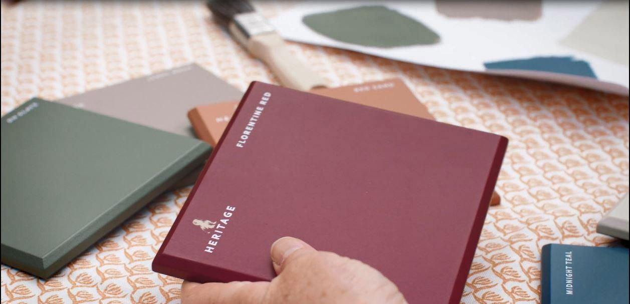 A person holding a book of paint colors on a table.