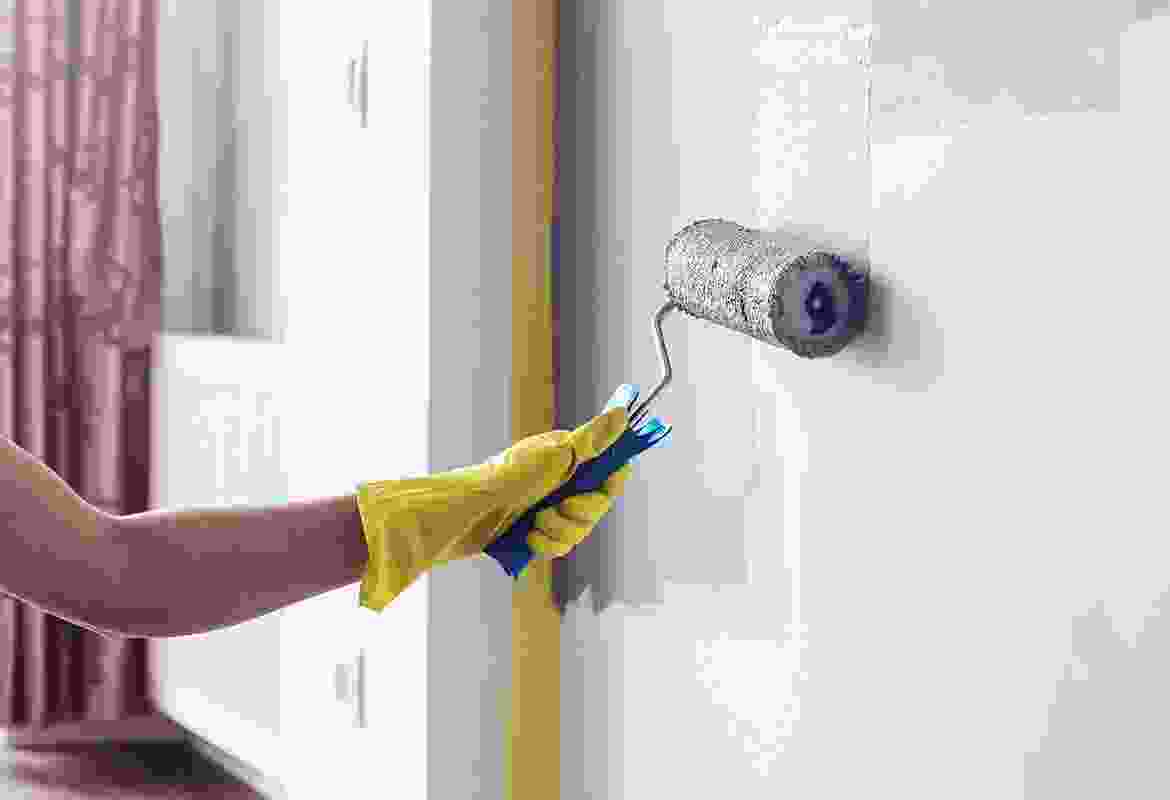 A woman is painting a wall with a paint roller.