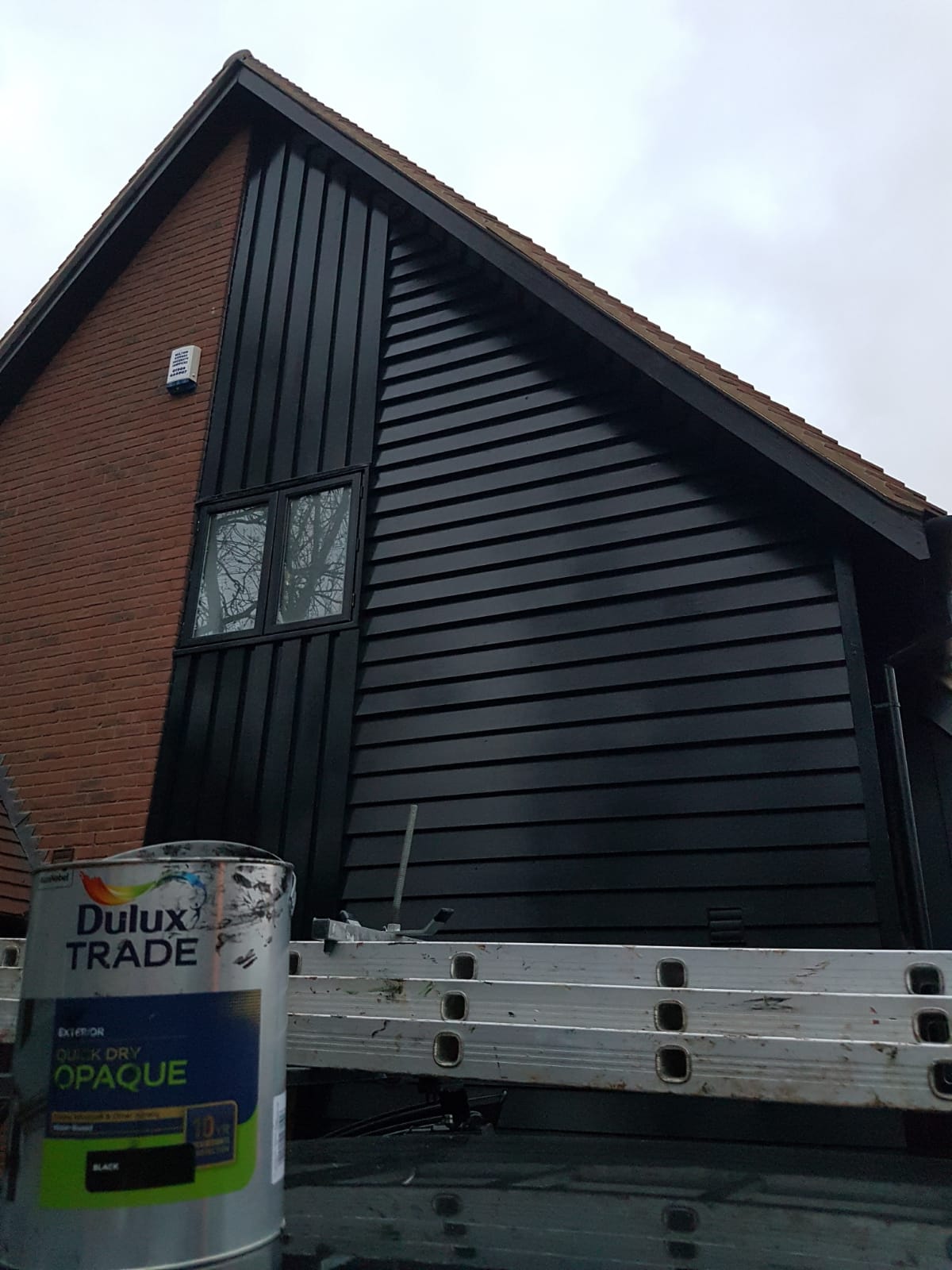 Black cladding on a house with a can of paint.