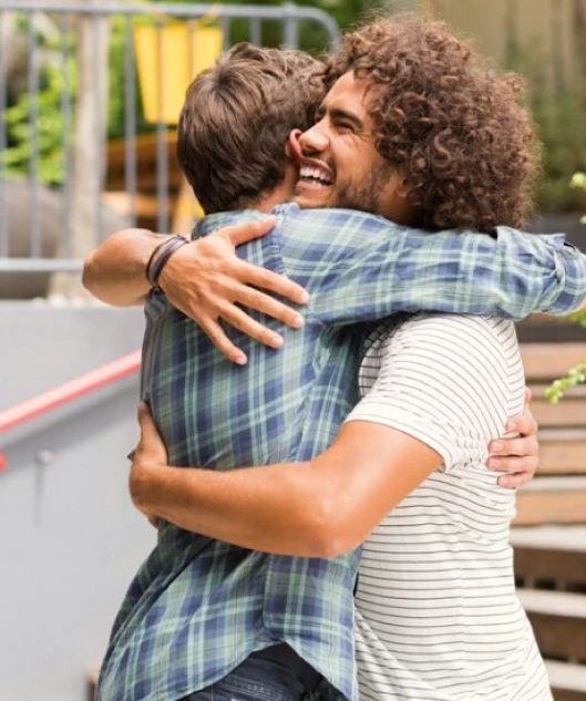 Two men hugging and smiling outdoors.