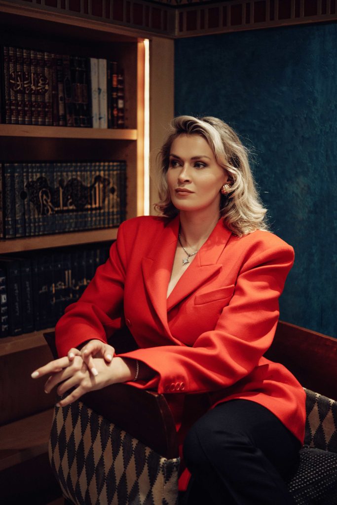 Person in red blazer sitting near bookshelf.